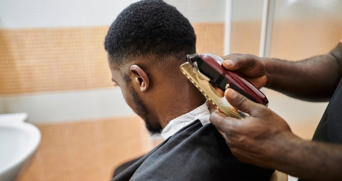 homem negro cortando seu cabelo com um barbeiro no estilo mid fade
